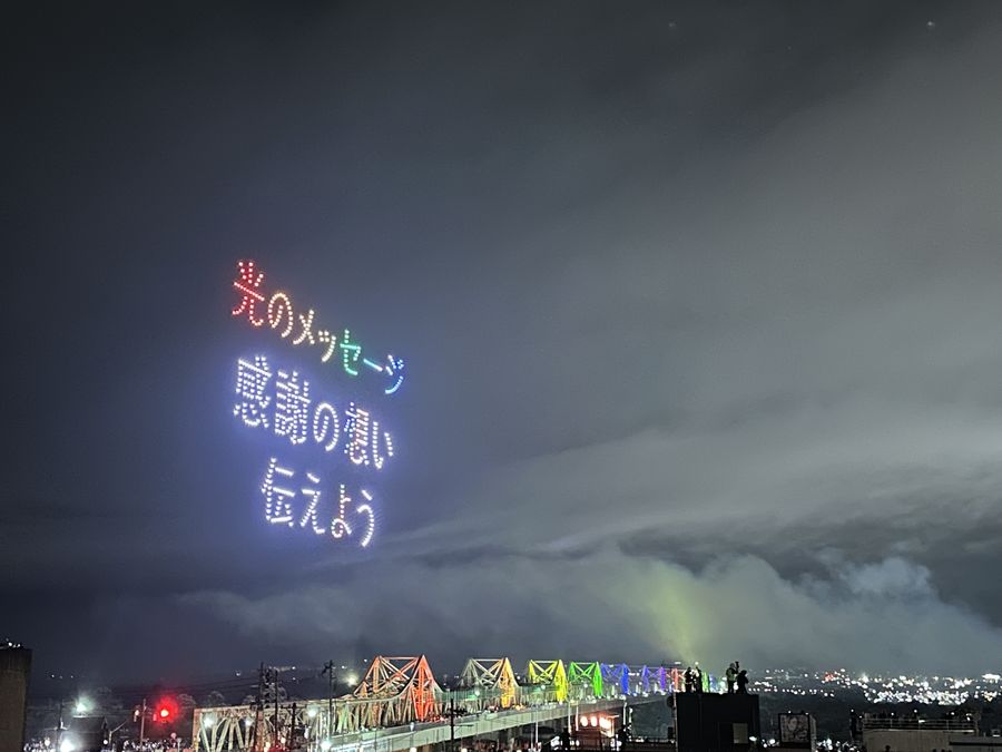 夜空に浮かぶ光のメッセージと、虹色にライトアップされた長生橋